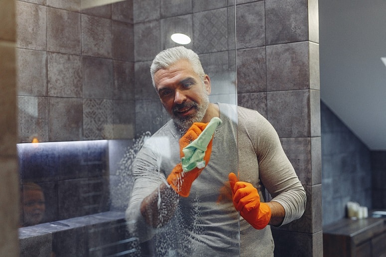 Grey haired man happily cleaning in the bathroom.