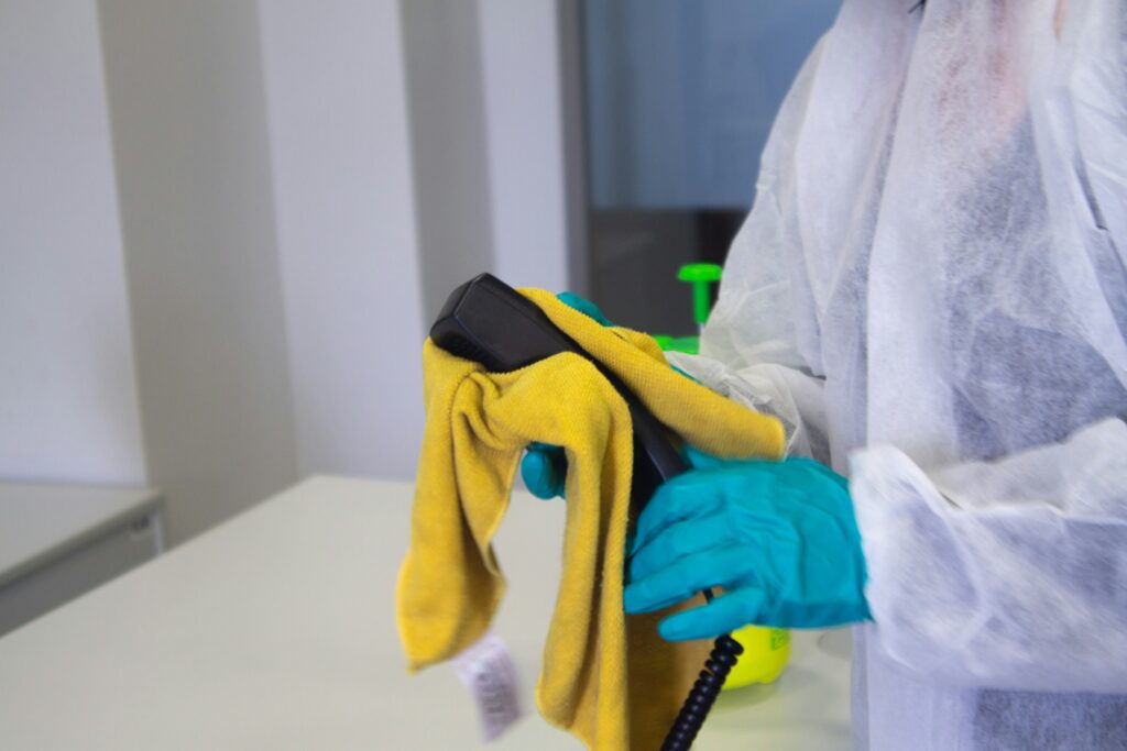 person-in-protective-suit-and-gloves-disinfecting-office-phone-with-yellow-cloth